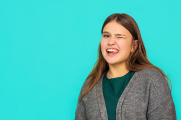 Obraz premium Headshot Portrait of happy teenage ginger girl with smiling looking at camera. Blue background. portrait of a pretty young woman winking