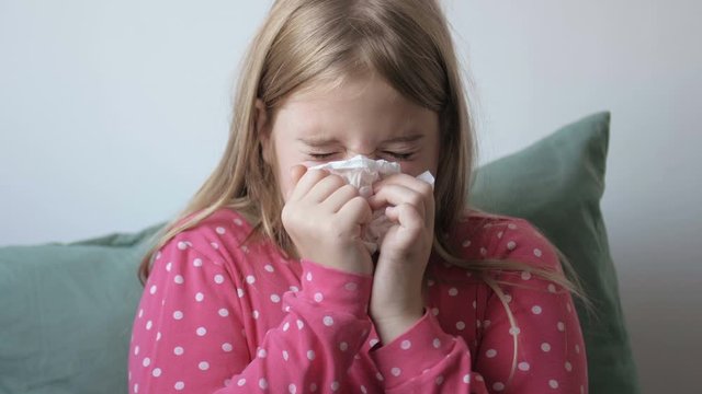 Sick caucasian girl blowing nose with a napkin. Cute child suffering from rhinitis and coughing