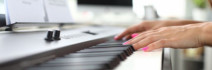 Focus on sensual female hands playing on synthesizer by notes. Woman with bright pink nail polish. Modern workplace on blurred background. Musical art concept