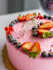 Homemade pink birthday cake decorated with berries: strawberries, blueberries, red currant and flowers. Food concept. Girl birthday or wedding cream cheese pink cake