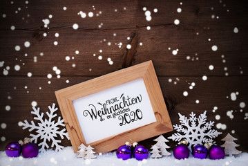 Fototapeta na wymiar Frame With German Calligraphy Frohe Weihnachten Und Ein Glueckliches 2020 Means Merry Christmas And A Happy 2020. Pruple Christmas Ornament Like Ball, Tree And Star. Wooden Background With Snow