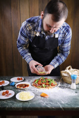 man preparing a pizza, knead the dough and puts ingredients