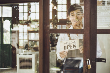 Store owner turning open sign broad through the door glass and ready to service.