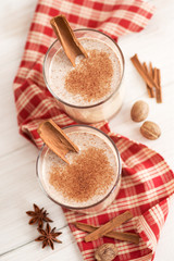 Eggnog in glass cups with a delicate foam, spices and a cinnamon stick