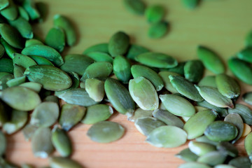 Pumpkin seeds scattered on a wooden background close up. Green color toned