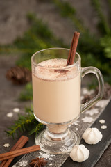 Eggnog in glass cups with a delicate foam, spices and a cinnamon stick