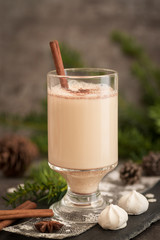 Eggnog in glass cups with a delicate foam, spices and a cinnamon stick