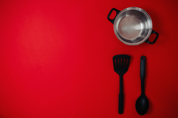 Black friday image with space for text. Bkack friday sale flat lay. Banner for home goods shop. Silver saucepan, spatula, big spoon on the red background.