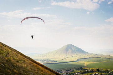 A paraglider flies in the sky in a cocoon suit on a paraglider over the Caucasian countryside with...