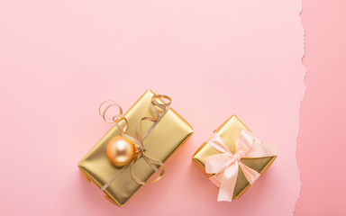Festive boxes with satin ribbon bow golden toy balls a pastel pink background. Flat layout. Holiday concept. Copy space.