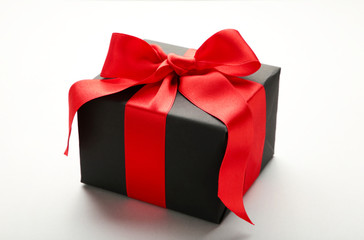 Black gift box with red ribbon and bow on grey background.