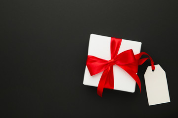 White gift box with red ribbon with sale tag isolated on black background