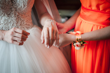Bridesmaid in orange dress helps bride to wear bracelet