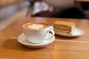 Cup of coffee and a piece of honey cake on wood table, close-up.