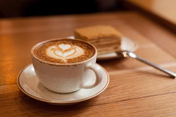 Cup of coffee and a piece of honey cake on wood table, close-up.