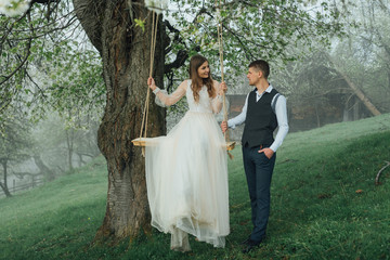 The bride and groom ride a rope swing in the garden. Wedding in the forest.