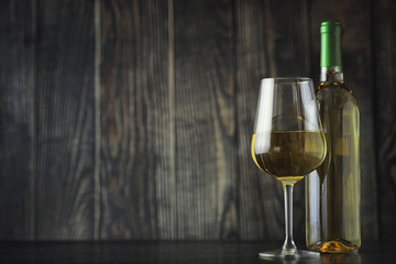 Transparent bottle of white dry wine on the table. White wine glass on a wooden background.