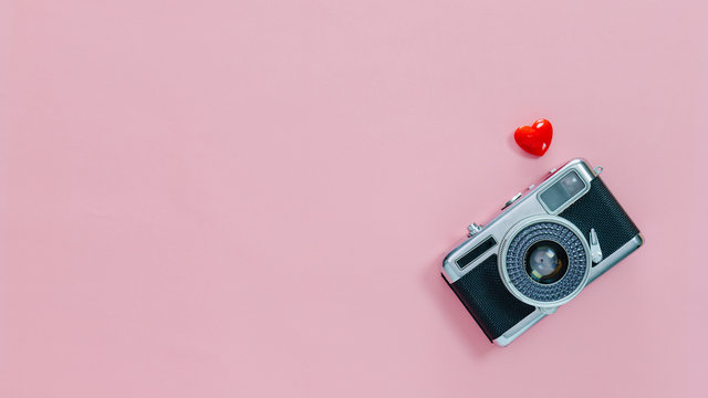 Top view of vintage old camera and little red heart on pink pastel background with empty space for text.Travel in holiday vacation with retro banner concept.