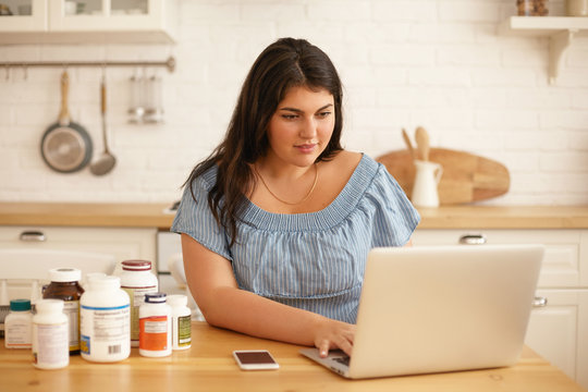 Attractive Plus Size Young Woman Blogger Working From Home Office, Writing Reviews Online On New Dietary Supplements For Body Shape And Weight Loss On Her Account Via Social Network, Using Laptop