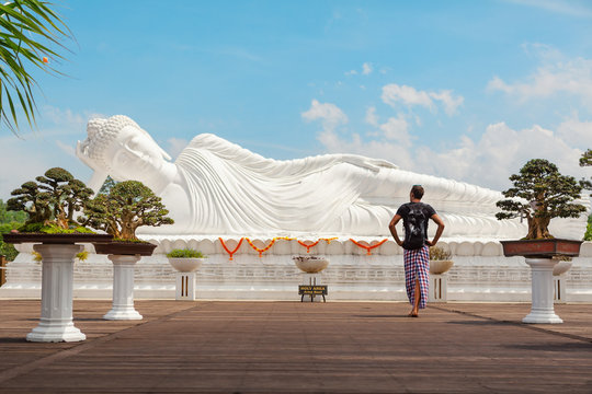 Young man travel in Bali, Indonesia. Tourist walk in buddhist temple Vihara Dharma Giri, see at lying Buddha statue. Popular travel destination background. Art, culture, religions of Indonesian people - Powered by Adobe