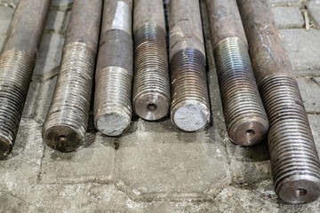 A large threaded rod lies on the floor in the workshop.