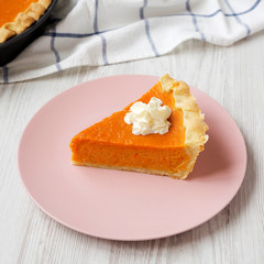 Homemade Thanksgiving pumpkin pie on a pink plate on a white wooden background, low angle view. Closeup.