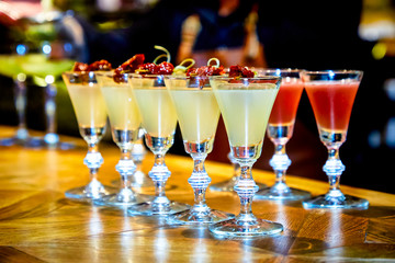 The bartender pours yellow cocktails into shots on a high leg on the bar