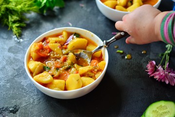 Photo of food on a dark background. Children's hands and food. The child holds hands a bowl with vegetable stew. Baby is having lunch. Food on a concrete background.
