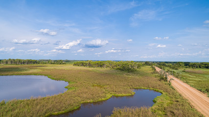 Aerial view of Transpantaneira dirt road along a typical lagoon and meadow landscape, with blue sky, Pantanal Wetlands, Mato Grosso, Brazil