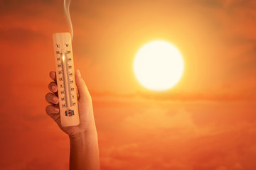 Hand holding the thermometer with high temperature on the air with glowing sun background