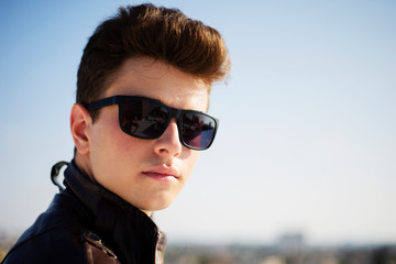 Young attractive man posing in front of camera in a dark  brown jacket on the roof of a residential building