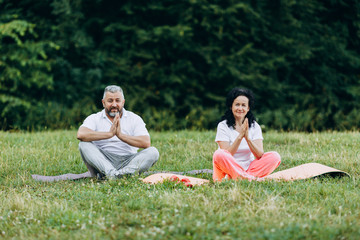 Middle age woman and man  doing yoga together outdoors making gesture namaste.-   Image