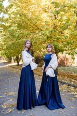 Obraz na płótnie Canvas Two very beautiful young ladies in fashionable blue dresses in autumn park.