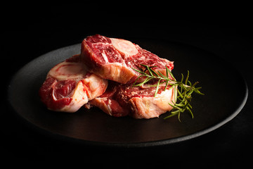 Osobuco carne cruda sobre un plato redondo negro y un fondo negro liso. Vista de frente