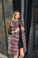 Style and fashion. Blonde woman in fur coat standing near reflecting doors