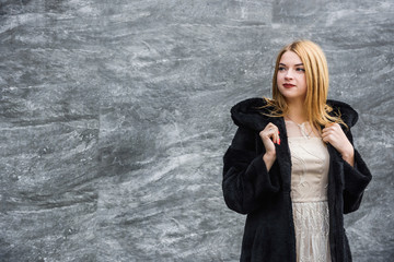 Portrait of fashion woman. Beautiful woman in fur coat posing on dark wall background