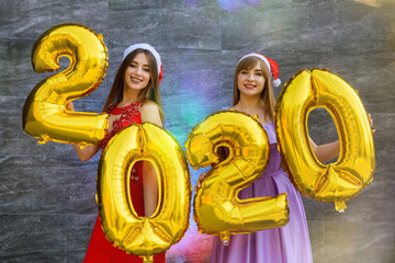 Portrait of two smiling happy girls in christmas dresses posing with gold colored number balloons 2020