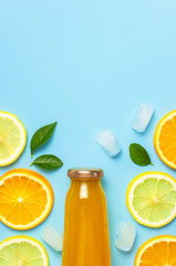 Flat lay composition with glass bottles of juice or fresh, slices of fresh lemon and orange, green leaves, ice cubes on blue background top view copy space. Citrus Juice Concept, Vitamin C, Fruits