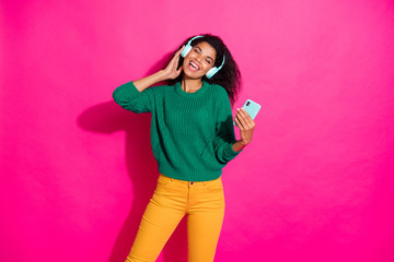 Portrait of cheerful positive girl with headset use smartphone listen stereo melody song sing on autumn fall vacation wear green pullover yellow trendy pants isolated pink color background