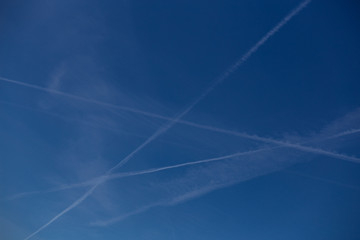 Blue sky with clouds, traces of airplanes draw diagonal lines in the sky