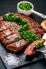 Ready to eat black Angus beef rib eye steak sliced with herbs, garlic and sauce on slate Board. Ready meal for dinner on black wooden background