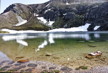 Fototapeta na wymiar Lago en las montañas con reflejos en el agua de montañas y nieve