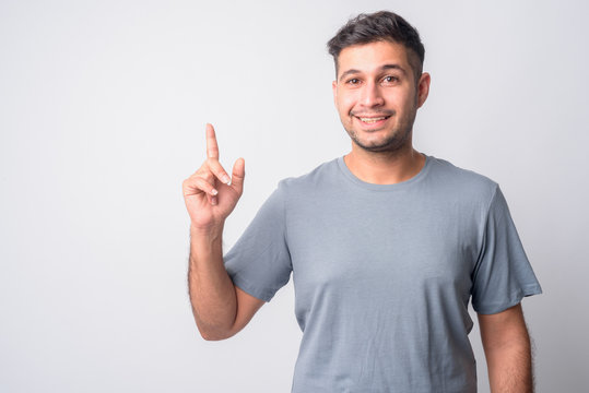 Portrait of happy young handsome Persian man pointing up