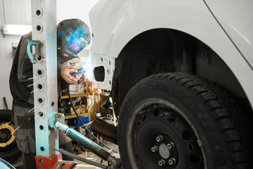 Auto mechanic in protective mask welds car body. Metalworking with carbon dioxide welding. Concept...