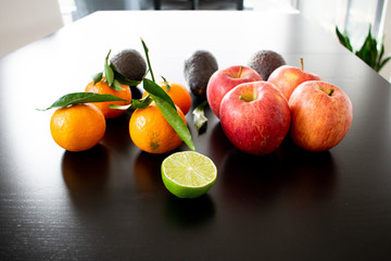 Arrangement of different healthy fruits and vegetables: apples, avocados, mandarine, lime, sweet potatoes. Shot on black background with light reflections. 