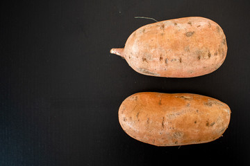 2 red sweet potatoes isolated. Shot on black background with light reflections. 