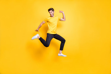 Fototapeta na wymiar Full body photo of handsome guy jumping high waving arm old friends on streets glad to see them wear casual t-shirt black trousers isolated yellow color background