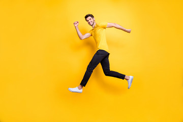 Fototapeta na wymiar Full length photo of handsome guy jumping high speed running competition participant rushing shopping wear casual t-shirt black trousers isolated yellow color background