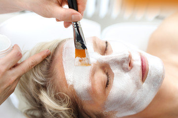 Woman in a beauty salon. The beautician puts a silver mask on the woman's face