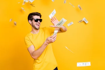 Fotobehang Photo of young handsome careless guy throwing money banknotes away wealthy person wear sun specs casual t-shirt isolated bright yellow color background © deagreez